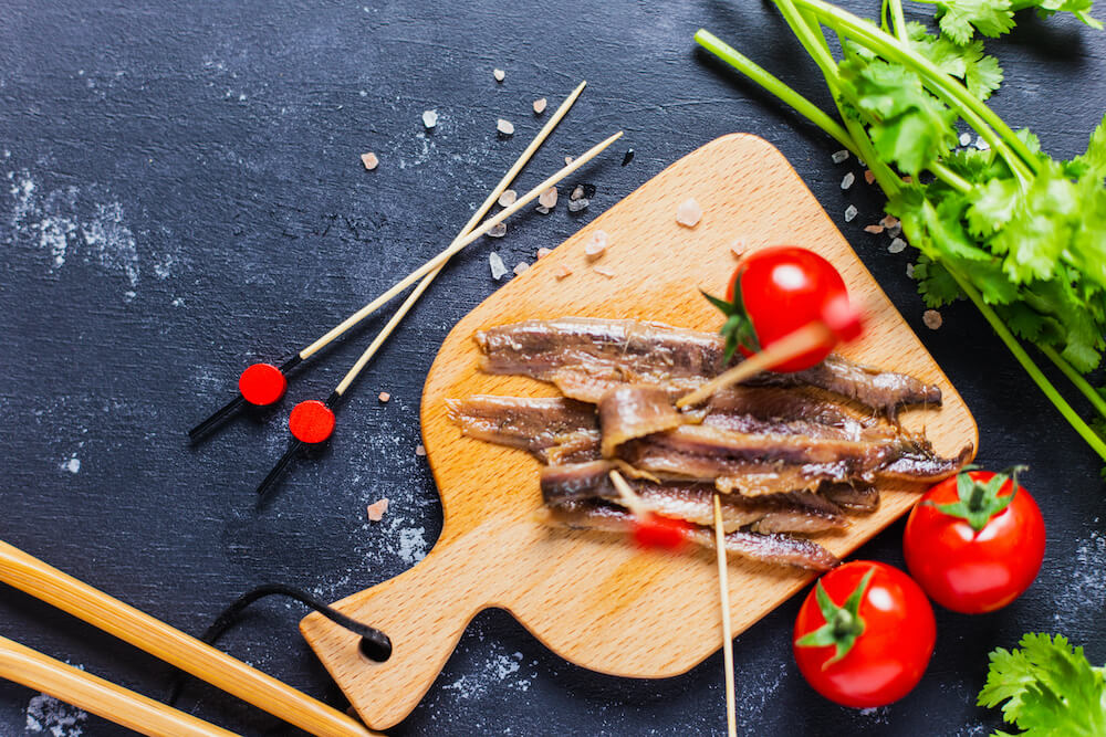 anchois nabite na wykałaczkę położone na desce anchois na drewnianej desce z pomidorami