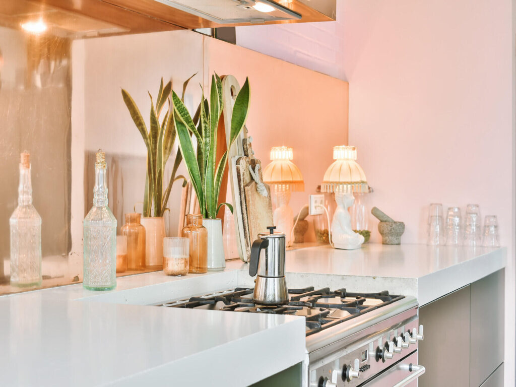 Kolory farb do kuchni - jasna kuchnia z pastelowym kolorem ścian i kwiatem doniczkowym Kolory farb do kuchni - przytulna, jasna kuchnia z białymi blatami